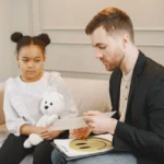 Uma criança segurando um brinquedo de pelúcia escuta um homem em uma sessão de terapia.